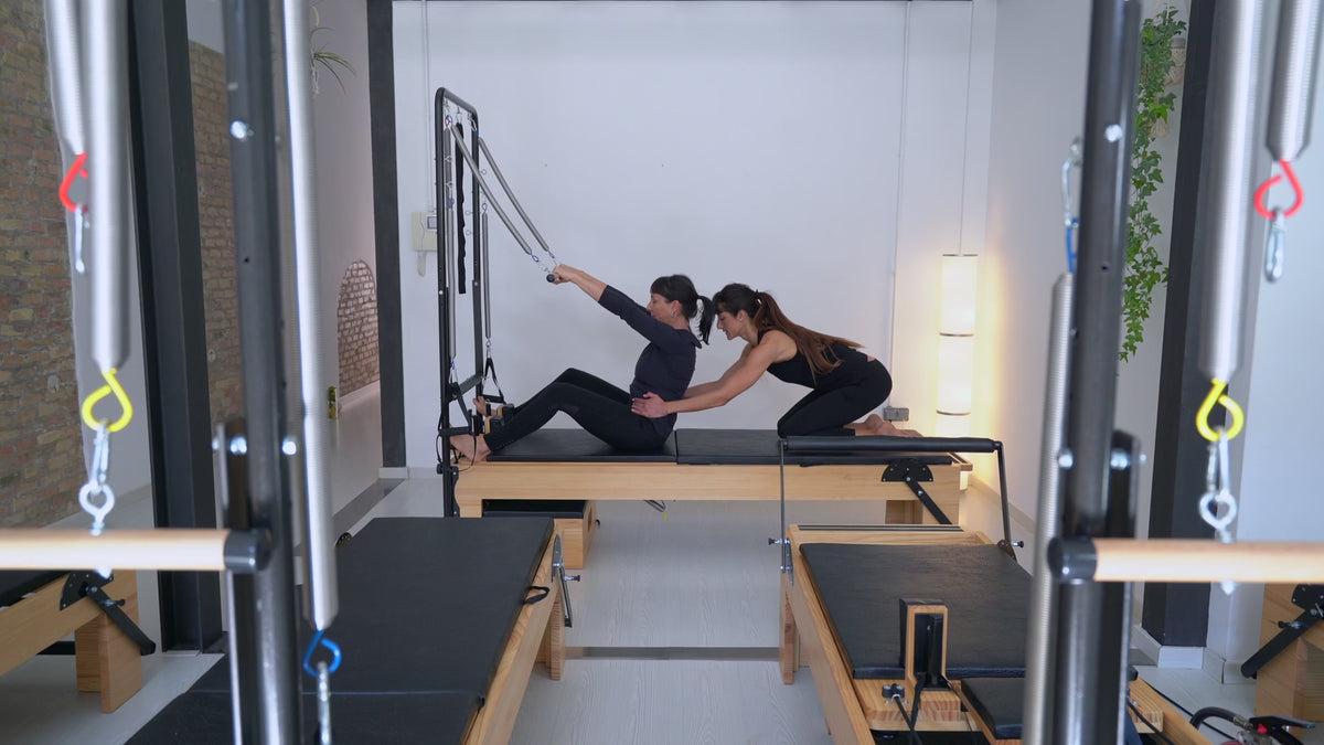Load video: Instructor-led work on a reformer with tower in a studio setting